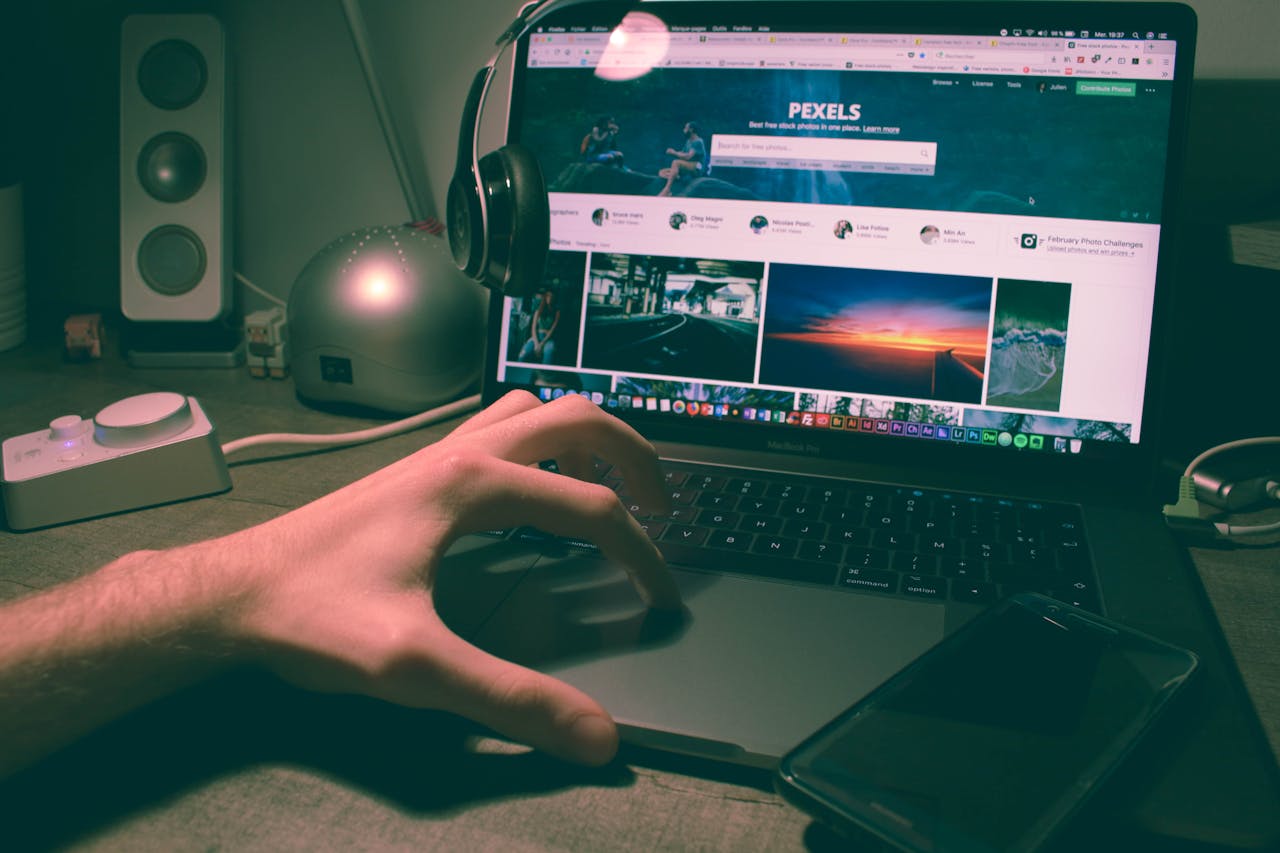 Person browsing Pexels on a laptop with headphones and smartphone nearby.